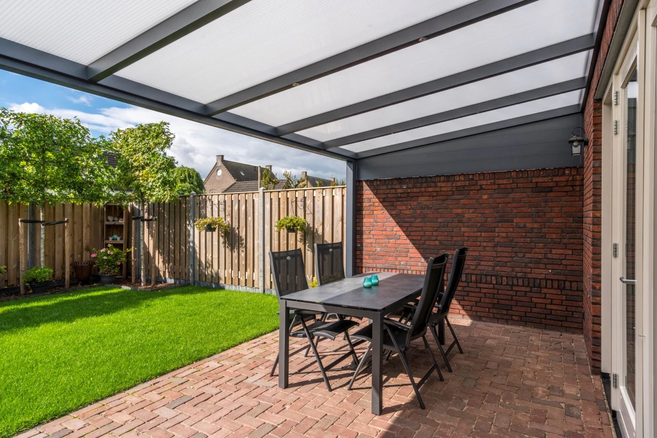 Aluminium side wall closing in a paved patio alongside a red-brick Dutch-style house with black dining set