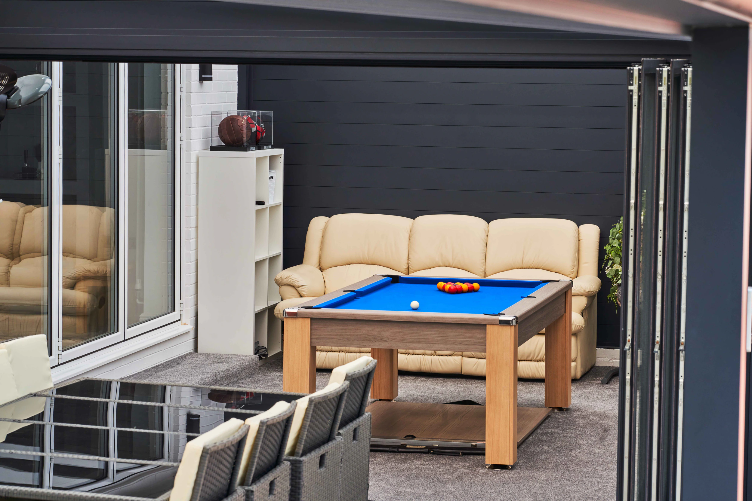 Aluminium side wall creating a games room under a veranda with pool table and cream leather sofa