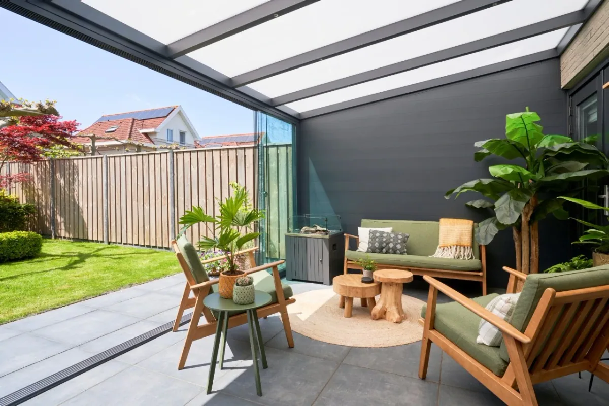 Anthracite aluminium side wall enclosing a garden veranda with wicker lounge chairs and potted tropical plants