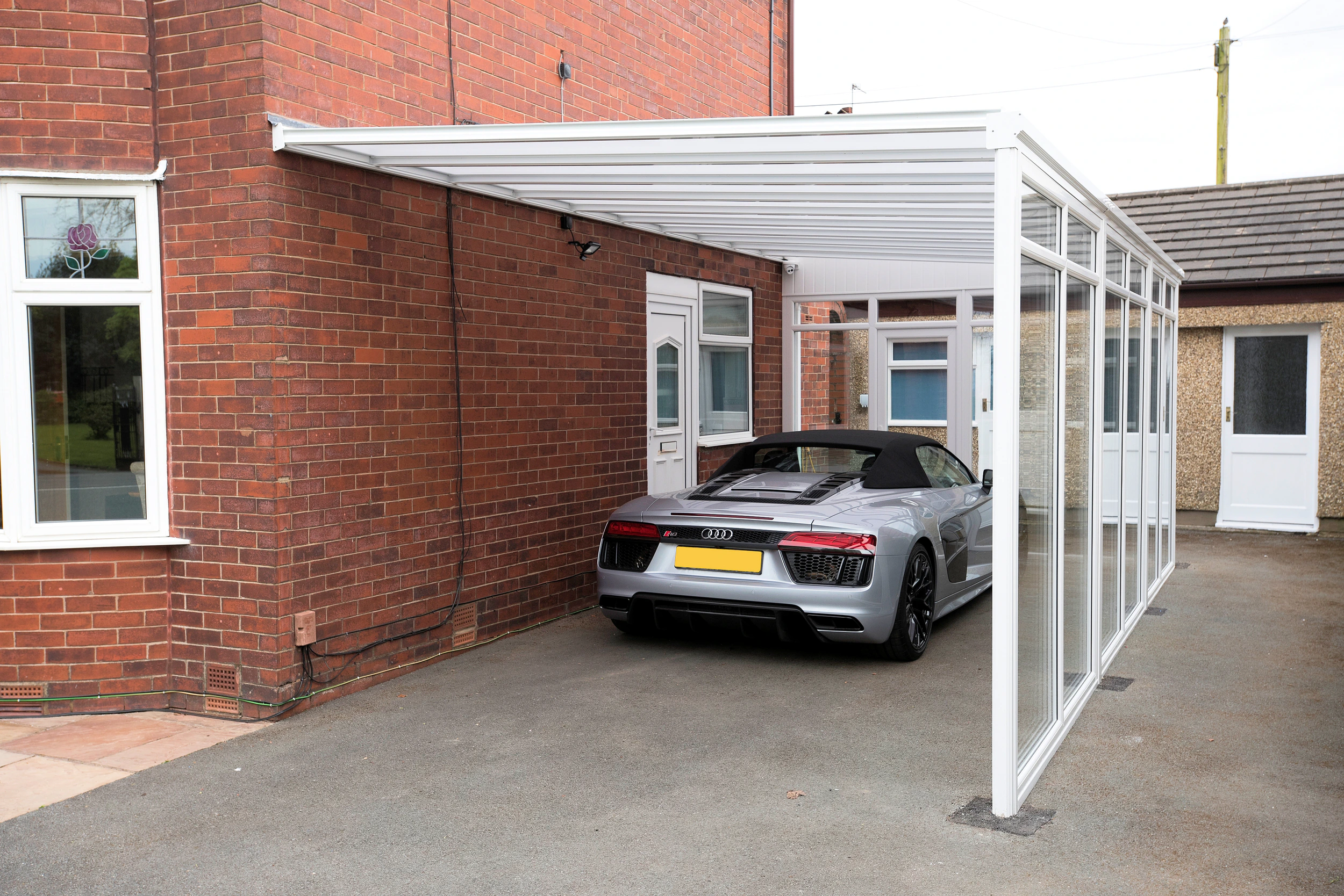 White fixed glass wall panels enclosing the side of a carport covering a silver sports car