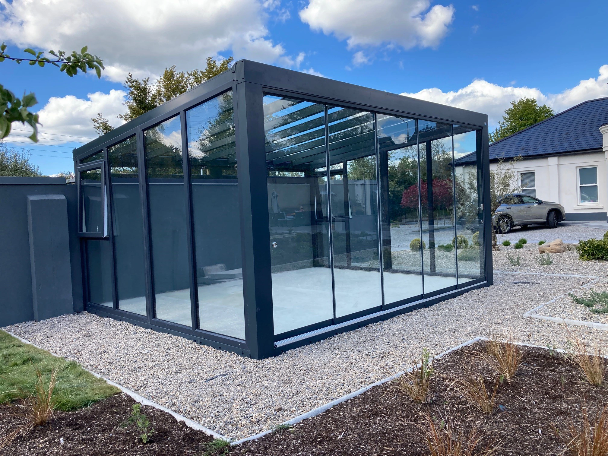 Free-standing fixed glass wall garden room with anthracite frame situated on a gravel driveway