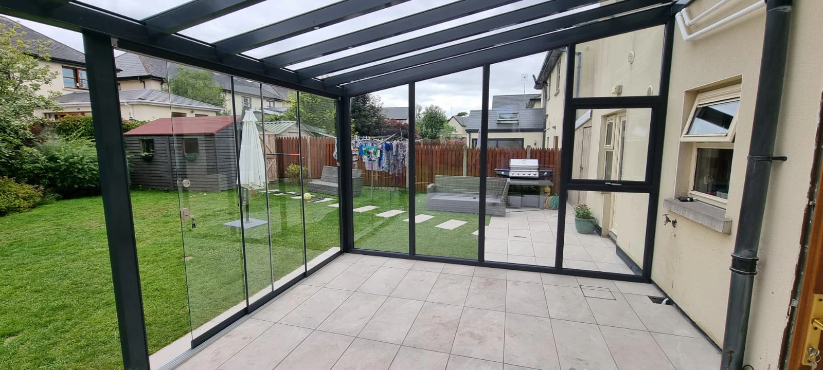 Interior view of a fixed glass wall garden room with anthracite frames, tiled floor, and garden outlook