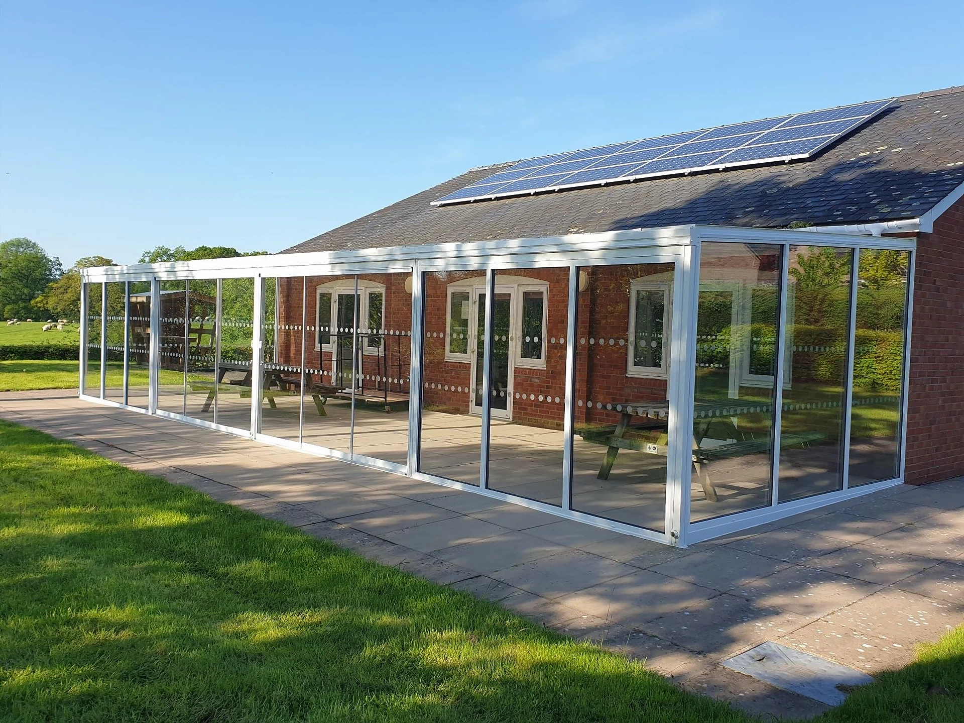 White fixed glass wall veranda along a red-brick bungalow with solar panels on the roof