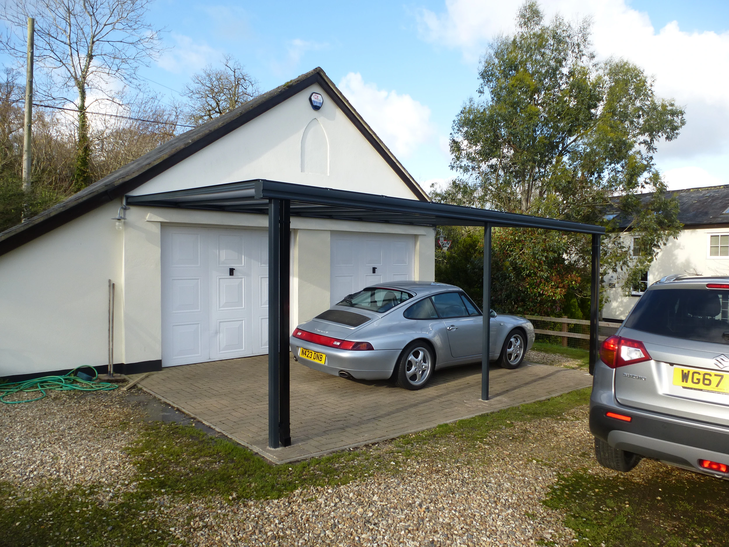 Harbour anthracite aluminium carport covering a driveway with a silver Porsche by a double garage