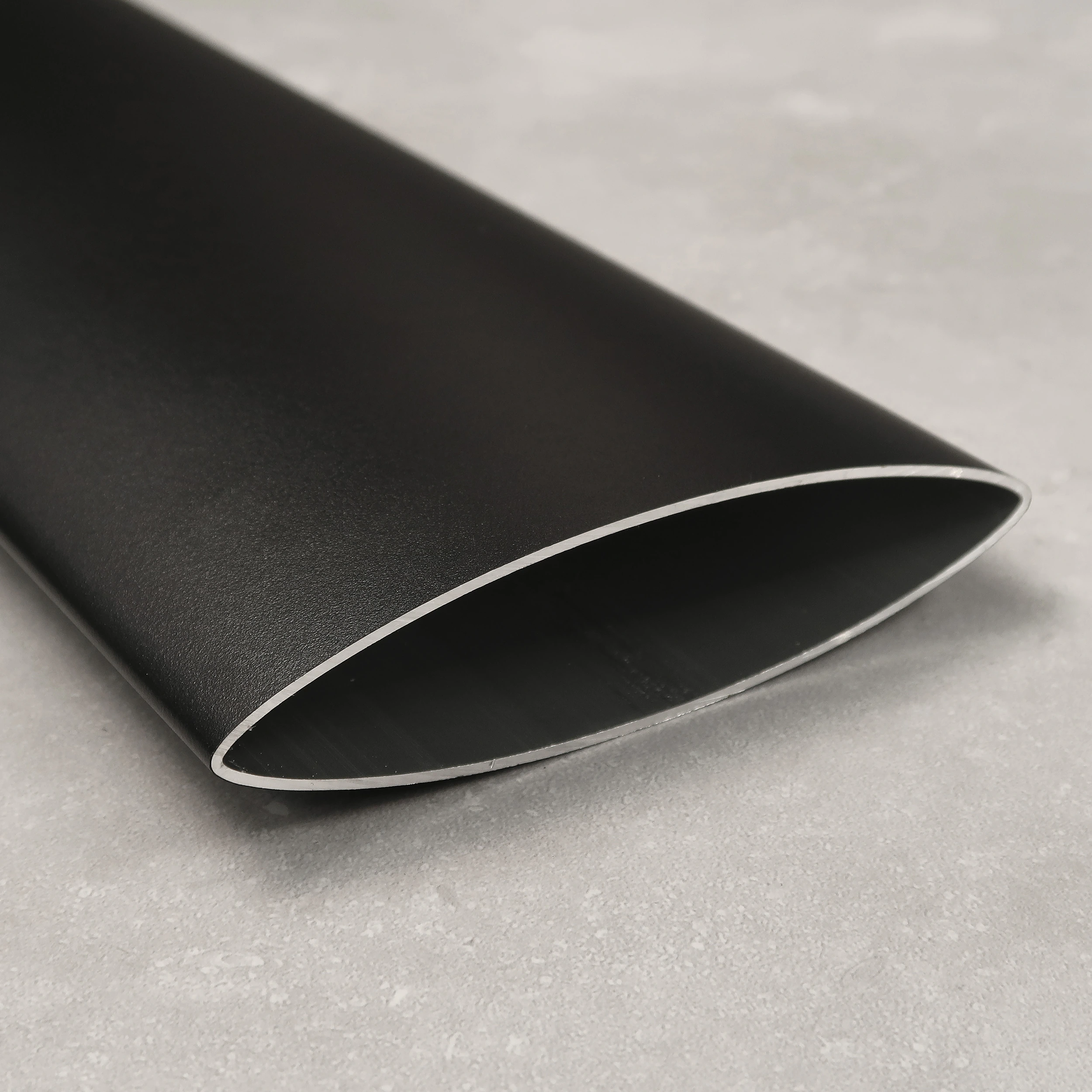 Product detail of an anthracite aerofoil-shaped louvred wall aluminium tube resting on a polished concrete surface