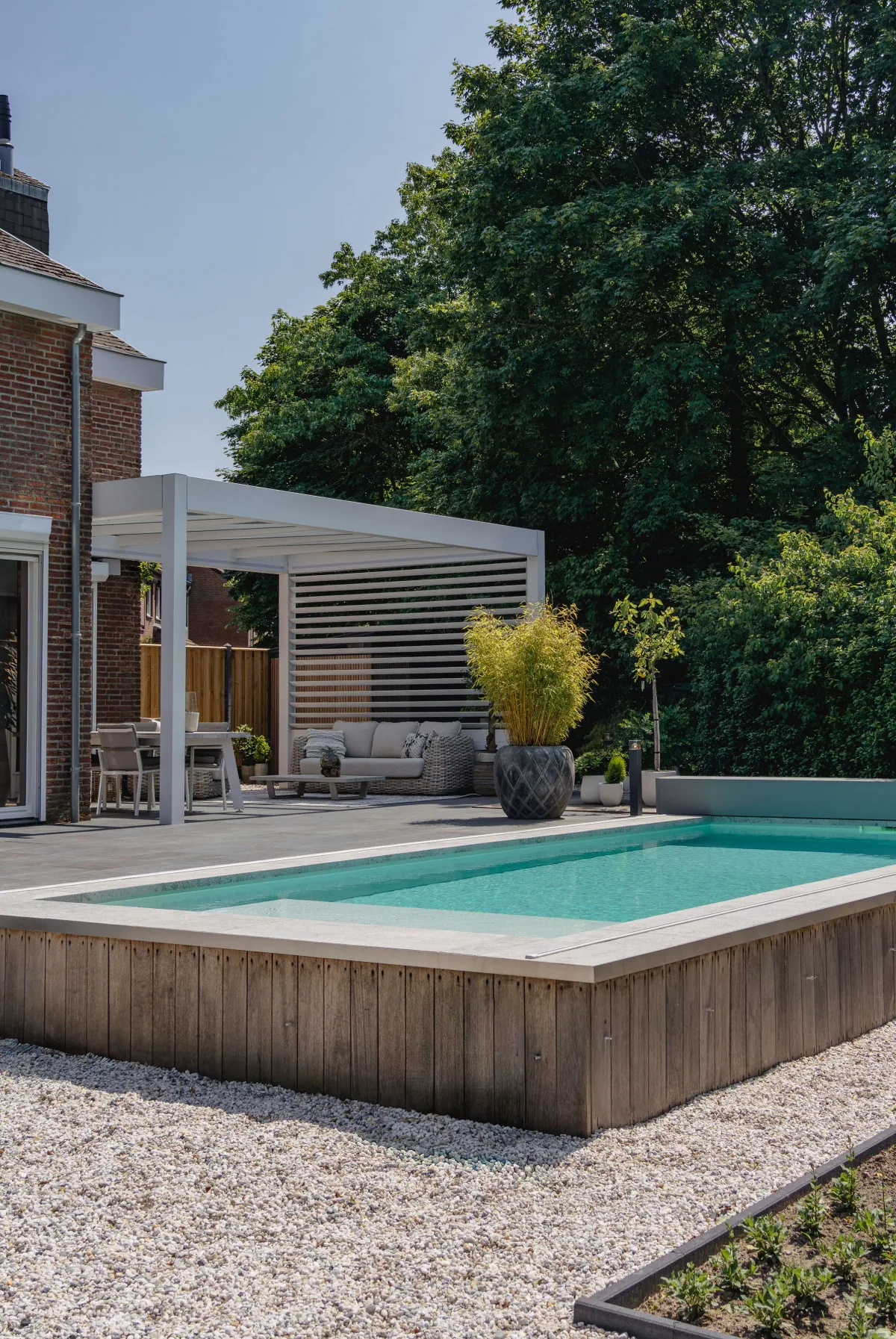 White louvred wall pergola beside a garden swimming pool with wooden decking and outdoor seating