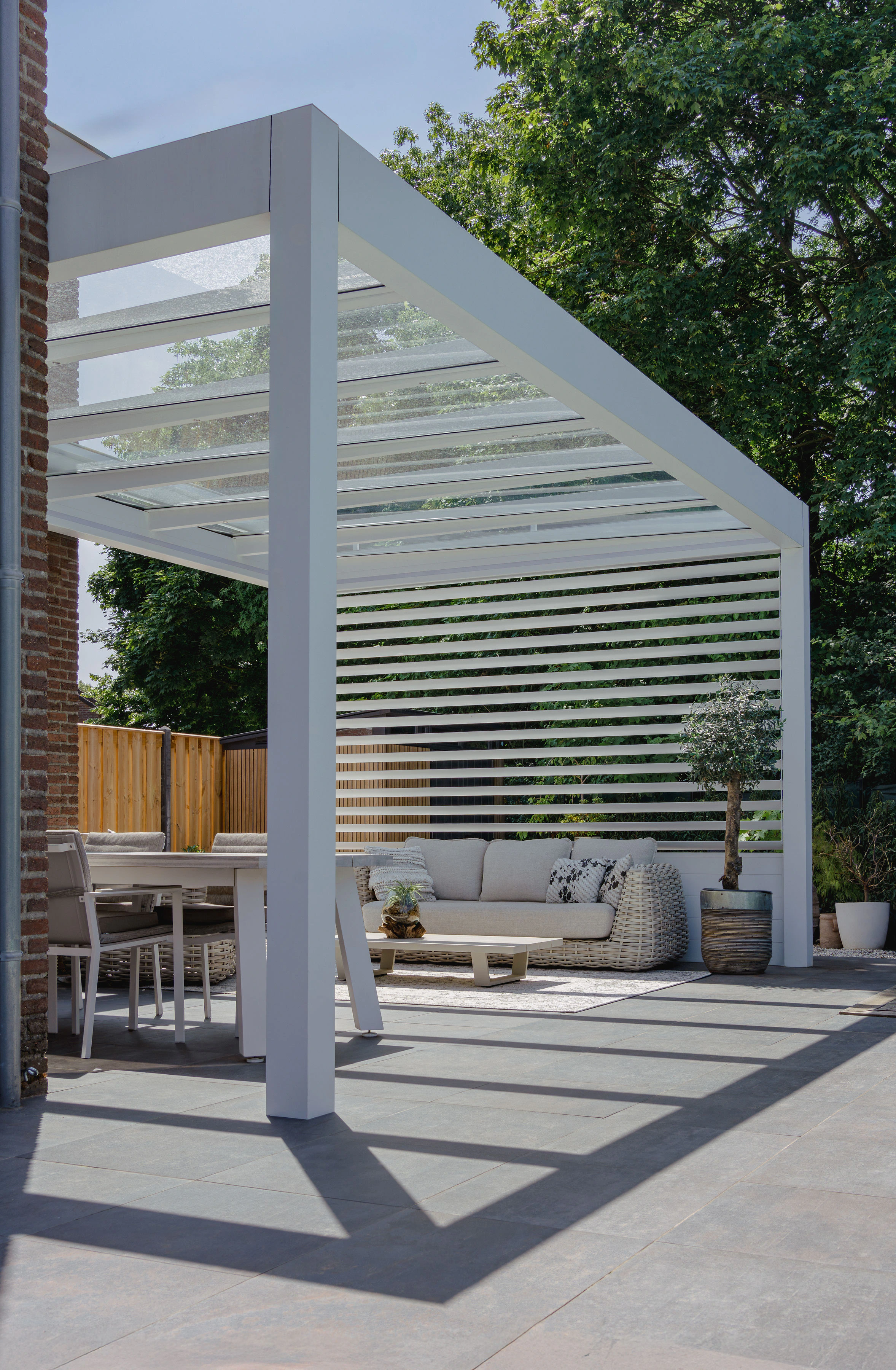 White louvred wall pergola creating a dappled shaded seating area with dining set and sofa on a tiled patio