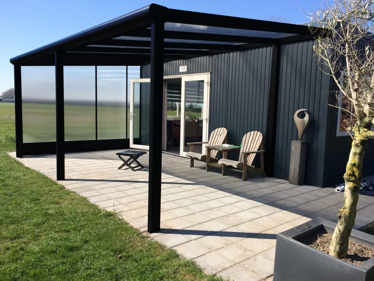 Black-framed veranda with polycarbonate side walls on a Dutch-style home with terrace and wooden deckchairs