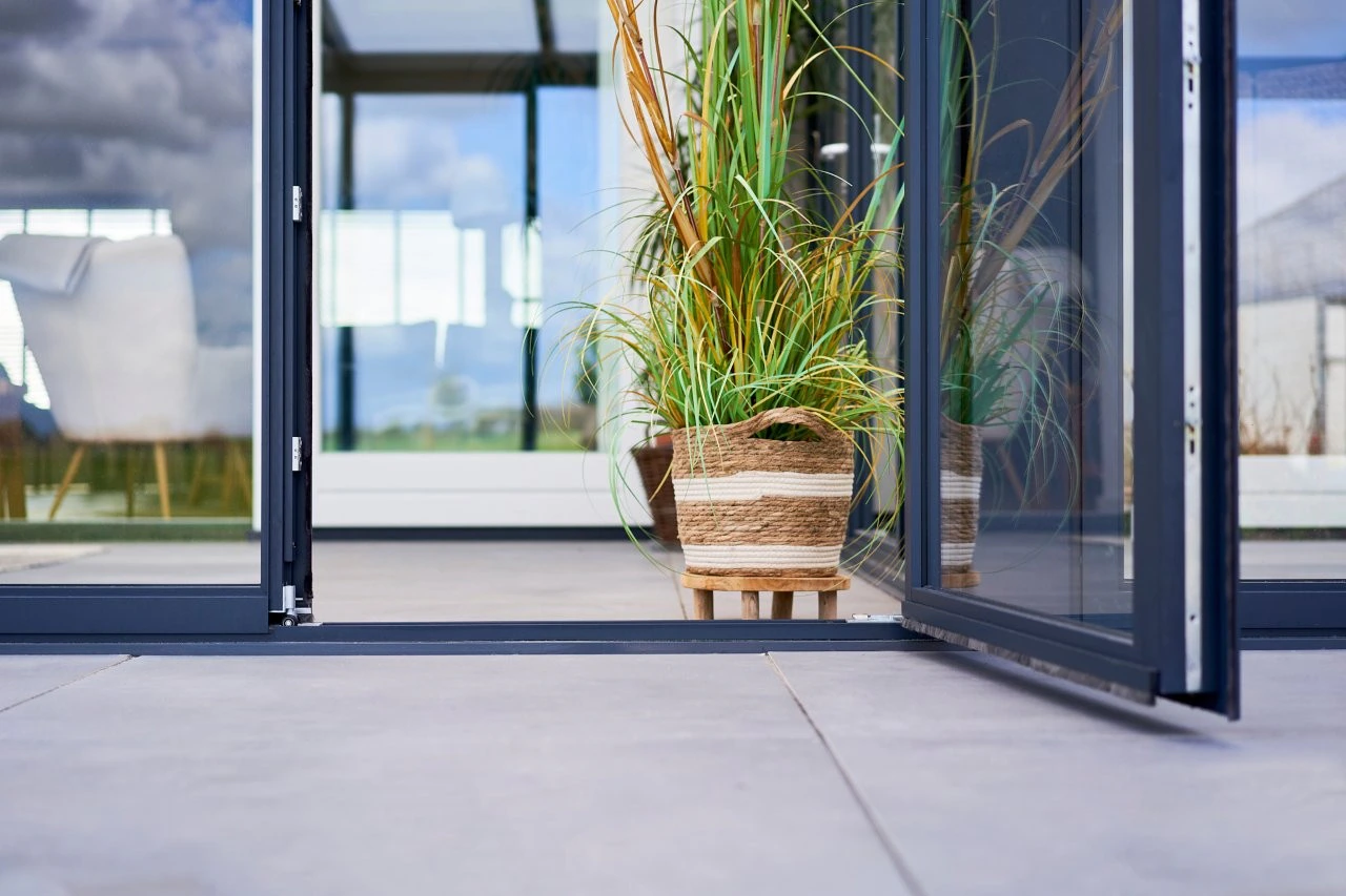 Close-up of slide and tilt glass panels opened outward with a potted ornamental grass on a concrete patio