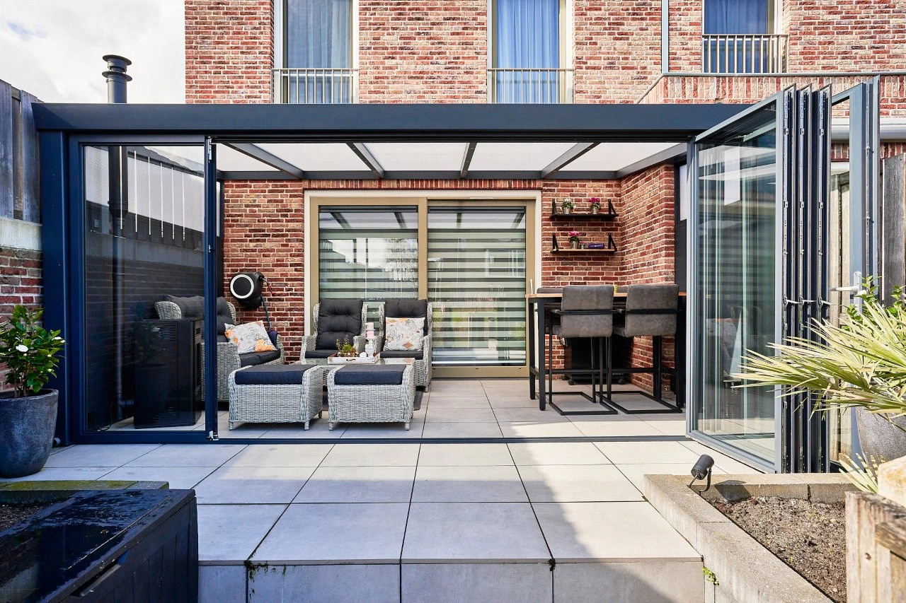 Slide and tilt glass panels opened across a veranda with outdoor bar and sofa seating on a paved patio