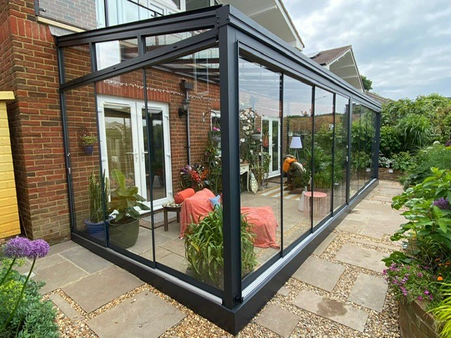 Black-framed sliding glass doors on a red-brick English home creating a fully enclosed garden room