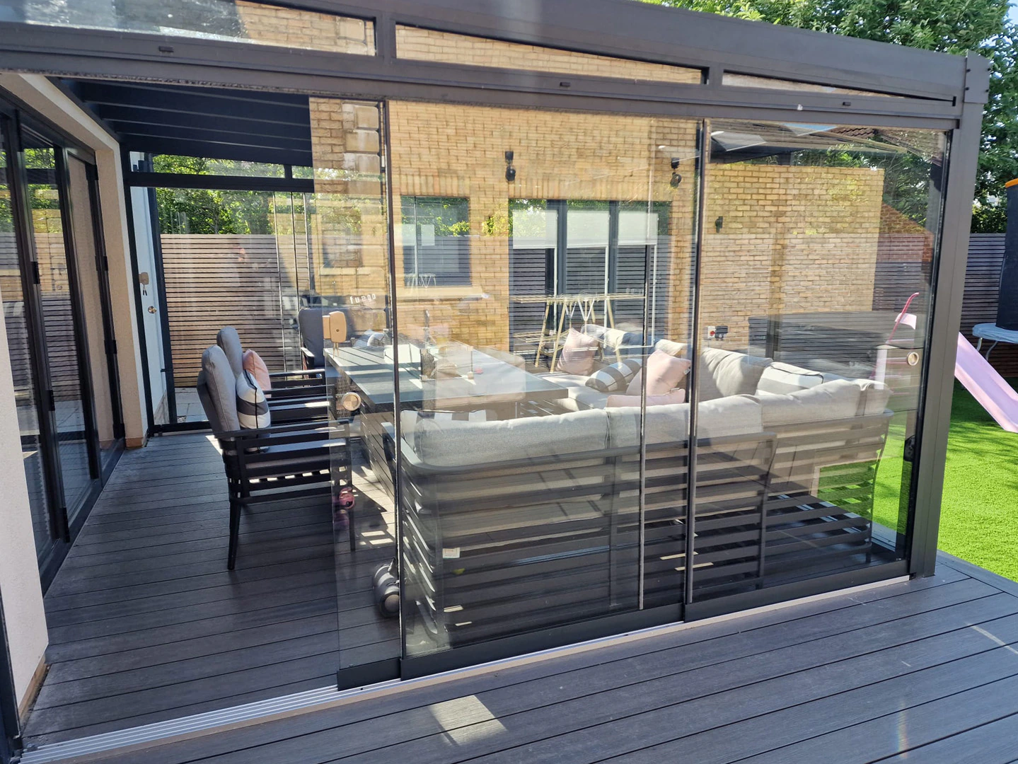 Sliding glass doors turning a veranda into a weatherproof garden room with sofa seating on composite decking