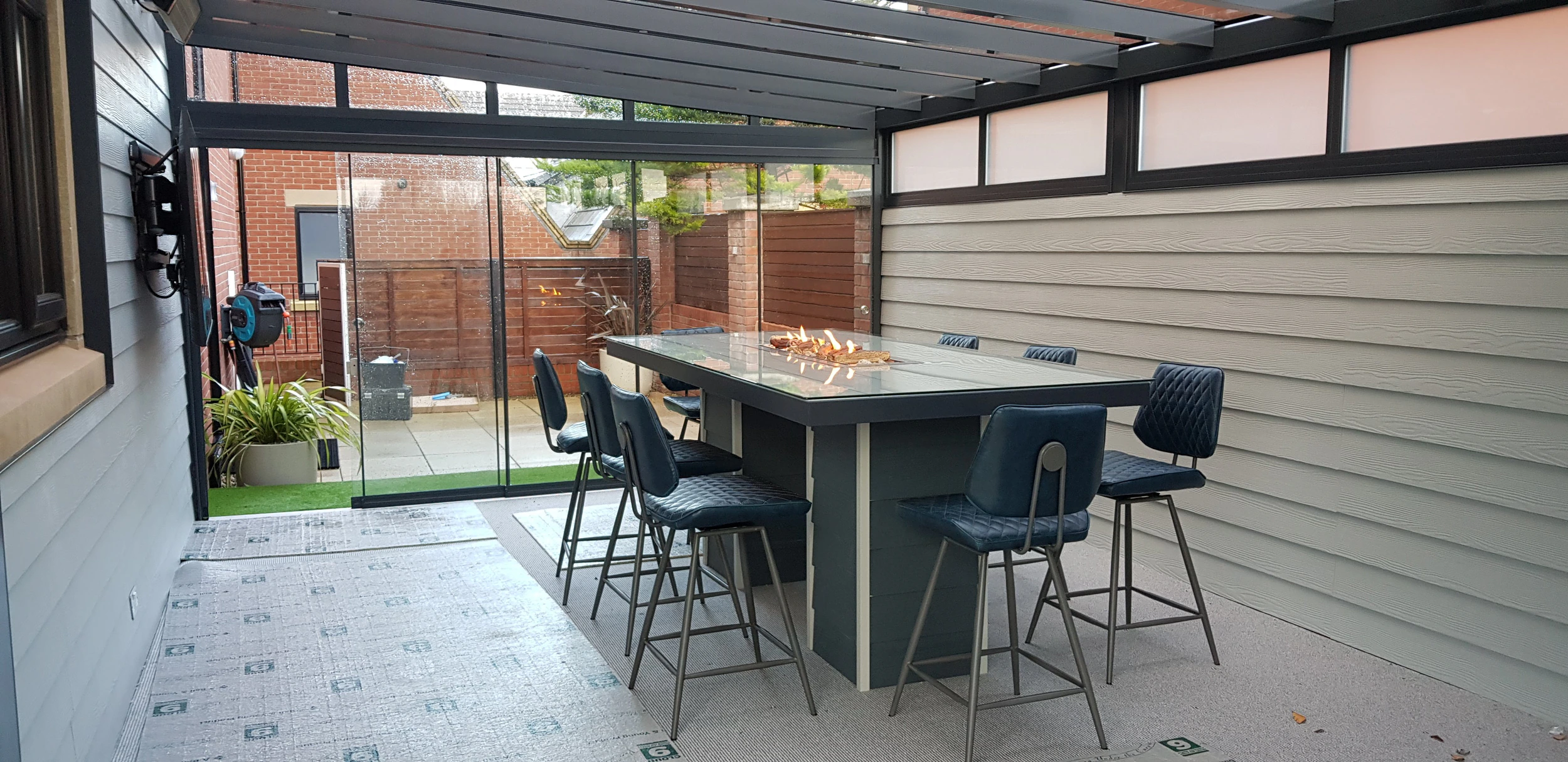 Sliding glass doors enclosing a veranda used as an outdoor bar with firepit table and bar stools