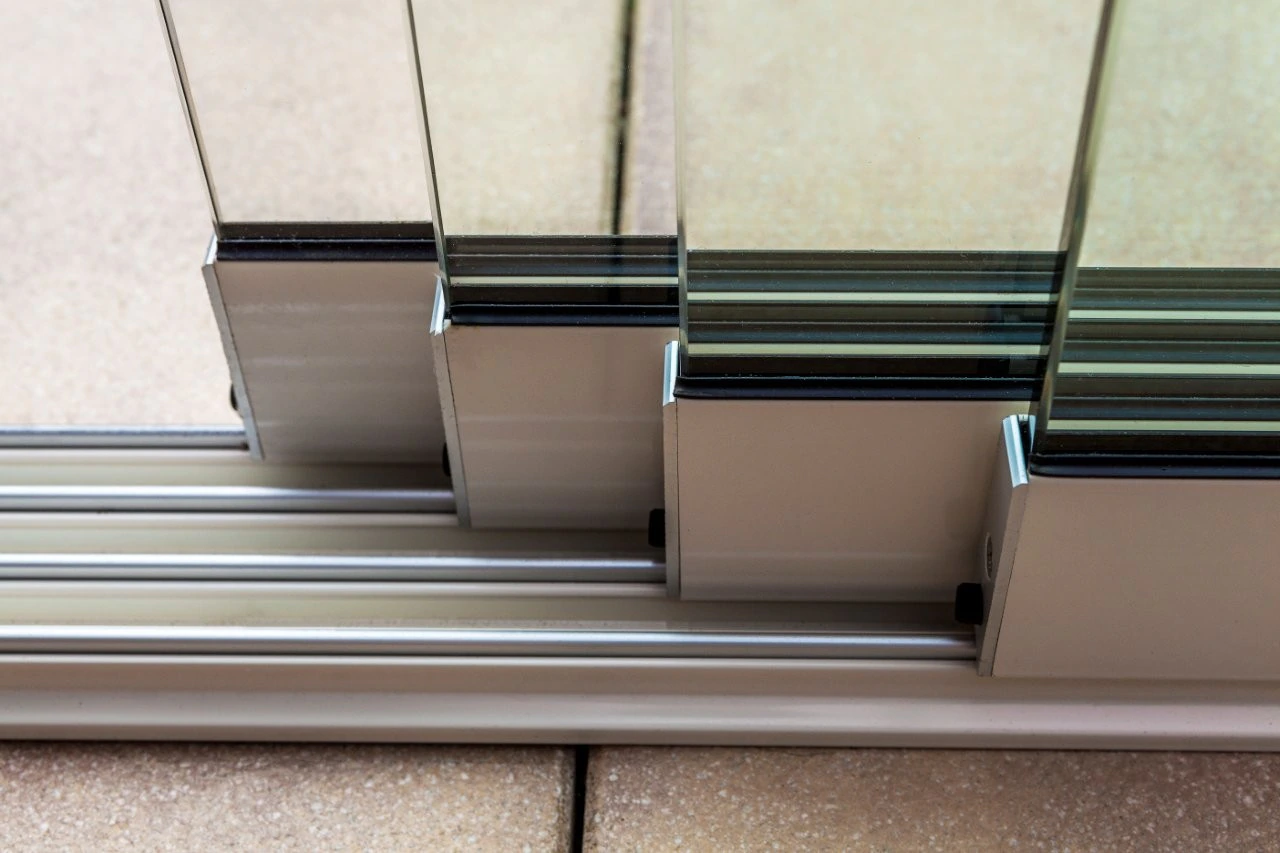 Close-up of aluminium multi-track sliding glass door system showing chrome rollers and toughened glass panels